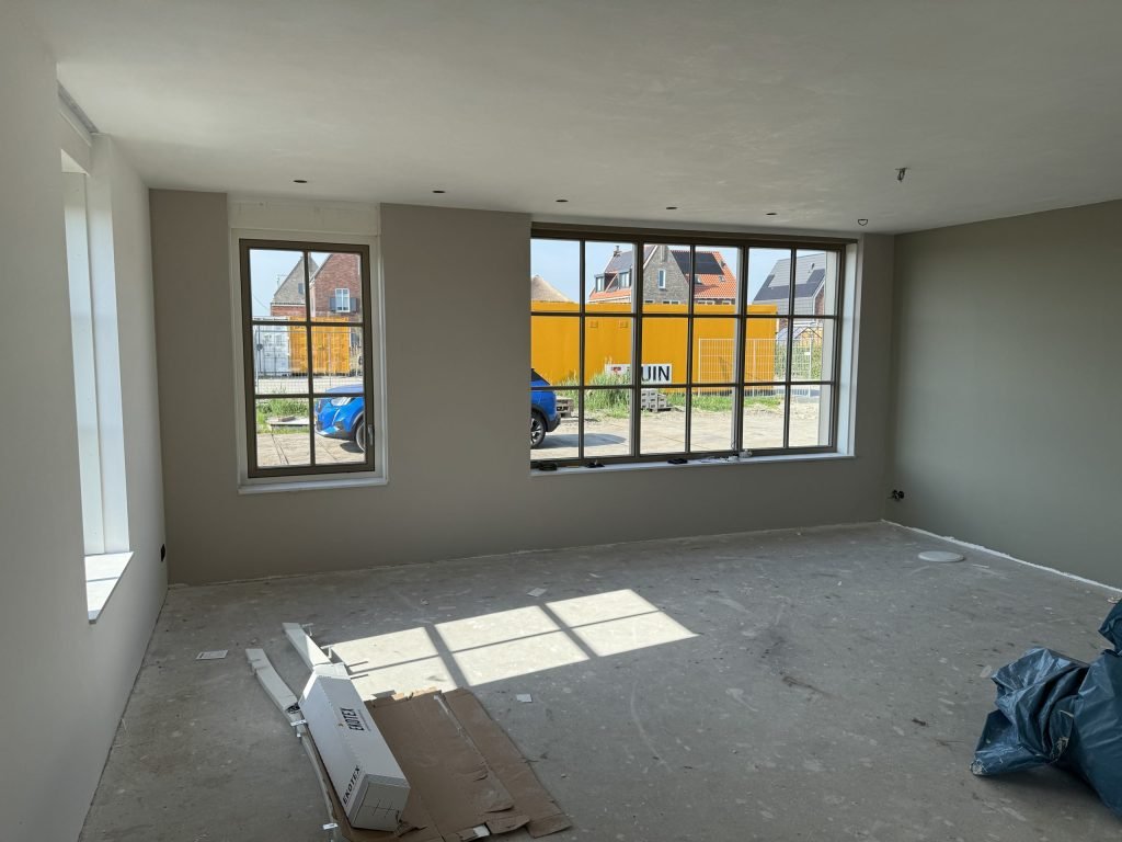 Woonkamer met roedenramen en een wand in grijsgroen, net na het sauzen