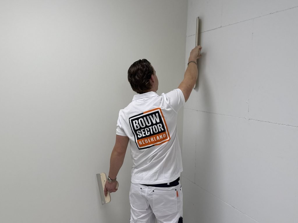 Vakman controleert met een rei of de wand vlak genoeg is